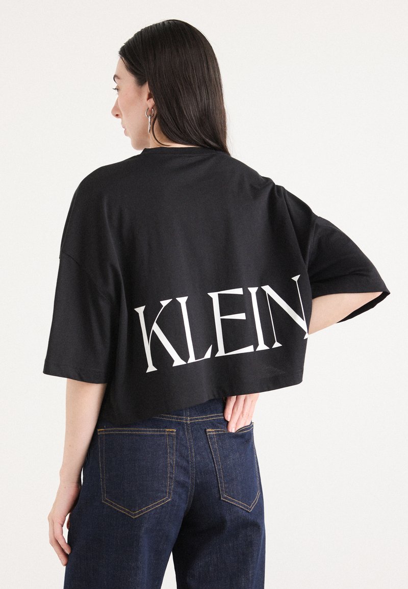 Černé croptop tričko s oversize střihem, na zadní straně s výrazným bílým nápisem "KLEIN". V kombinaci s tmavými džíny.