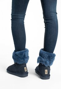 Stivali in suede blu scuro con un morbido e soffice risvolto in pelliccia blu. Presentano una superficie texturizzata e una suola piatta in gomma. Etichetta con la lettera "G" sul tacco.