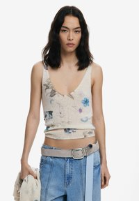 Ärmelloses Strickoberteil in Creme mit bunten Blumenmustern. Hat einen tiefen V-Ausschnitt und einen gerippten Saum. Kombiniert mit hellblauen, geschnallten Jeansshorts.
