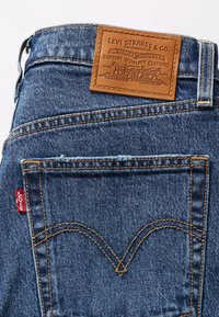Blå denimjeans bakficka med orange sömmar, röd Levi's etikett på sidan och en tan lädernit från Levi Strauss & Co. ovanför midjebandet.
