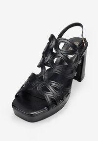 Black high-heel sandal made of smooth leather featuring cut-out designs, a closed back, and a platform outsole with a square toe.