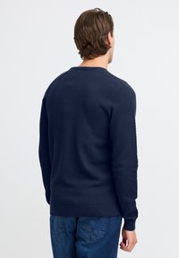 Navy blue textured sweater with a round neckline and ribbed cuffs, paired with denim jeans featuring back pockets.