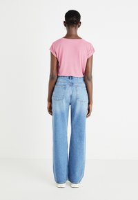 Tricou scurt cu mâneci scurte de culoare roz, combinat cu blugi ușor albastri, cu talie înaltă și picioare largi, prevăzuți cu buzunare pe spate și o textură netedă.