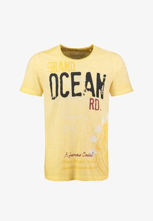 Camiseta amarilla de manga corta con un gran texto en negro y rojo, con un diseño texturizado y acentos sutiles desvanecidos. Incluye gráficos y patrones estilizados.