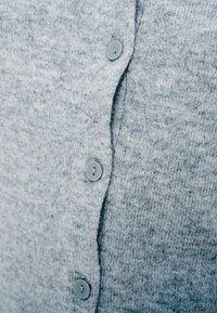 Γκρι πλεκτή ζακέτα με πέντε κουμπιά ίδιου χρώματος, ορατή υφή και ελαφρώς ανοιχτό μπροστινό ραφή. Μαλακό, μεσαίου βάρους ύφασμα.