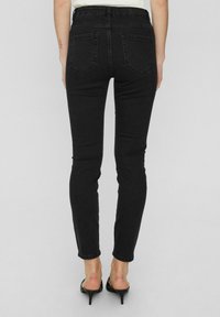 Czarne, wysokokotne skinny jeansy o gładkiej fakturze, z dwiema tylnymi kieszeniami i dopasowanym krojem, kończące się na kostce.