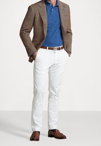 Brązowa marynarka w wzór jodełkowy, niebieski polo, białe spodnie, brązowe skórzane mokasyny. Akcesoria to brązowy pasek ze srebrną klamrą i ciemne skarpety.