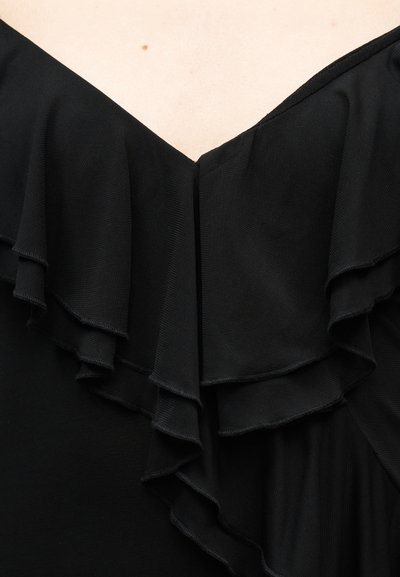 Μαύρο ρούχο με ανοιχτούς ώμους και πολλαπλές βολάν κατά μήκος του λαιμού σε ανοικτόχρωμο δέρμα.