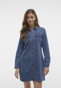Denimskjortklänning i mörkblått med långa ärmar, knäppning fram, två bröstfickor och en något krökt fåll. Slät textur.