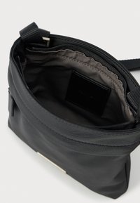 Czarna torebka na ramię z otwartą główną przegrodą, ukazującą szarą podszewkę i czarną prostokątną metkę wewnątrz.