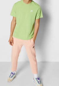 Zelené bavlněné tričko s bílým logem, spárované s světle růžovými tepláky s černým logem. Bílé tenisky s barevnými tkaničkami.