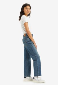 High-waisted blue denim jeans with a straight leg, subtle fading, and a classic five-pocket design. Paired with a plain white t-shirt and sneakers.