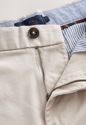 Beige raka byxor med metalldragkedja och knappstängning. Har ett blåmönstrat midjeband och randig innertyg.