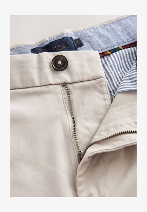 Beige raka byxor med metalldragkedja och knappstängning. Har ett blåmönstrat midjeband och randig innertyg.