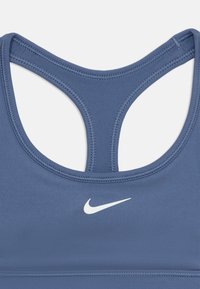 Modra atletska športna modrček z dizajnom racerback, gladko tkanino, ravnimi šivi in majhnim belim logotipom Nike na sprednji strani.