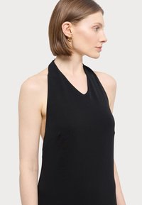 Svart halterneck topp med V-hals, tettsittende liv, og glatt stoff. Modellen har kort hår og bærer gull hoops øreringer.