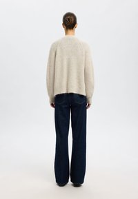 Overmaatse lichtgrijze sweater met een textuur gebreid, ronde halslijn en iets rafelrand, in combinatie met losse donkerblauwe jeans.