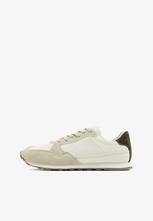 Lavprofil beige og hvid sneaker med ruskindsoverlejringer, snørelukning og mørkebrun hælaccents på en hvid baggrund.
