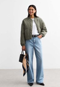 Quilted olive green bomber jacket, white shirt underneath, light blue wide-leg jeans, black handbag with a patterned scarf tied to it.