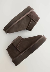 Braune Wildleder-Stiefeletten mit runder Spitze, genähten Akzenten, Gummisohle und glatter Oberfläche, die ein einfaches Design ohne Verzierungen aufweisen.