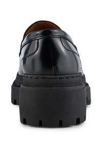 Zwarte leren schoenen met een ronde achterkant, een gestructureerde zwarte rubberen zool en een verhoging. Heeft zichtbare stiksels langs de naad.