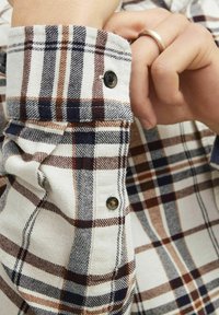 Flanellen shirt met een ruitpatroon in tinten van room, bruin en marineblauw. Opvallende details zijn de zwarte knopen en een keurig afgewerkt manchet.