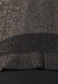 Närbild av ett metalliskt silver- och svart stickat tyg med ribbad textur vid fållen mot en slät svart bakgrund.