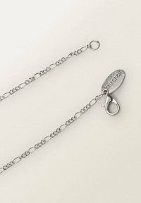 Chaîne en argent avec des maillons ovales, dotée d'un fermoir en forme de homard et d'une étiquette ovale gravée avec "SÉLECTION". Texture métallique lisse.