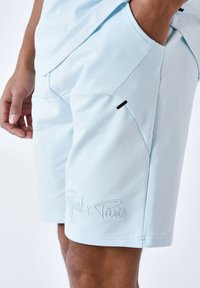 Pantaloni corti azzurri in un tessuto morbido, con una tasca laterale con un accento nero e un dettaglio ricamato "Project x Paris" sull'orlo.