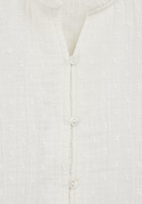 Weißer strukturierter Stoff mit einer vertikalen Reihe von vier kleinen, runden weißen Knöpfen und einem subtilen gepunkteten Muster über den gesamten Stoff.