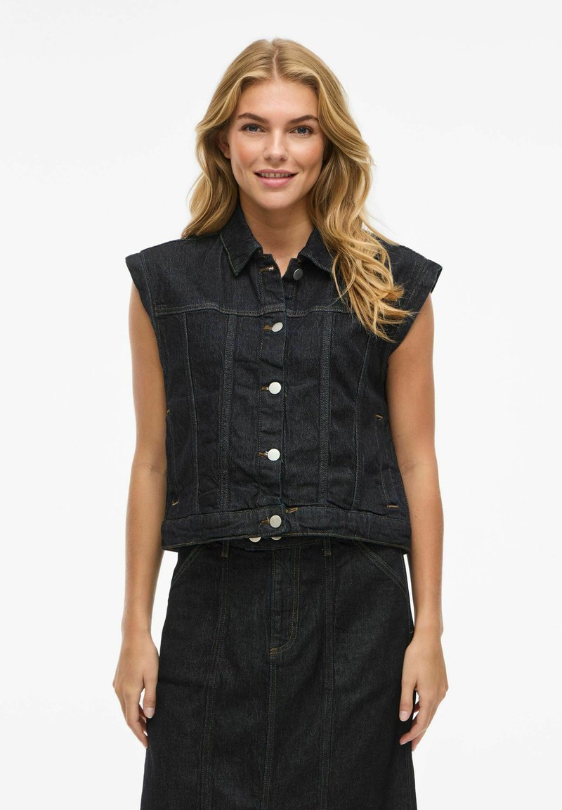 Mörk denim ärmlös jacka med krage, knapplist och lapplösa fickor. Har kontrasterande sömmar och en croppad design.