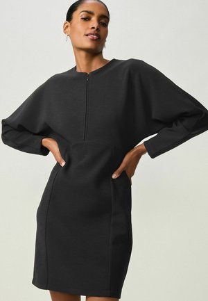 Abito nero con collo alto, maniche lunghe e oversize, e chiusura con zip. Realizzato in un tessuto liscio con una silhouette aderente e tasche laterali.