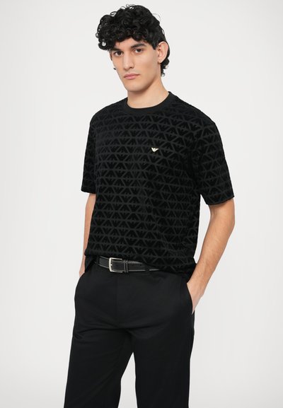 Čierne tričko z velvetu s textúrovaným vzorom prepojených trojuholníkov, s malým zlatým logom na hrudi. Krátke rukávy.