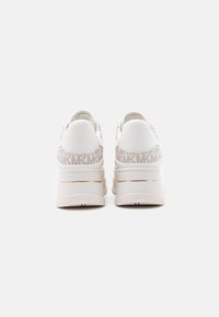 Ζευγάρι λευκά sneakers με πλατφόρμα και μπεζ μοτίβο "MK" στο τακούνι, με χρυσή ρίγα πάνω από την σόλα, από πίσω.