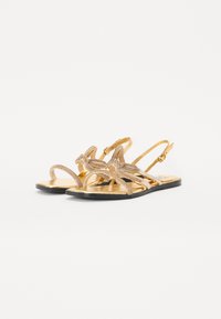 Gold flat sandals with a sleek design, featuring a glitter strap and a black sole. Adjustable slingback with buckle closure.