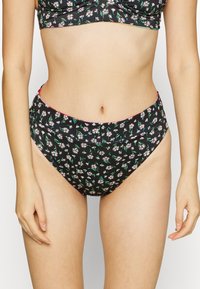 Svart bikinitruse med blomster mønster i hvitt og grønt, med høy midje-design og kontrasterende rosa detalj i midjen.