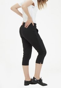 Pantalones recortados negros con un diseño elegante, que cuentan con una pequeña abertura en el dobladillo y una cintura elástica para mayor comodidad. Combinados con zapatos negros.