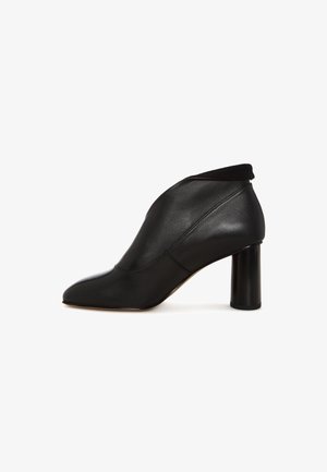 Czarny skórzany botek na obcasie, z ostro zakończonym czubkiem i masywnym obcasem, prezentujący elegancki, nowoczesny design na białym tle.