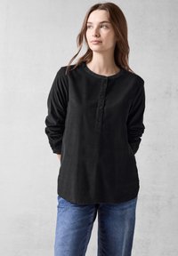 Maglietta nera a maniche lunghe con scollatura tonda, patta frontale con bottoni e vestibilità morbida, abbinata a jeans blu.