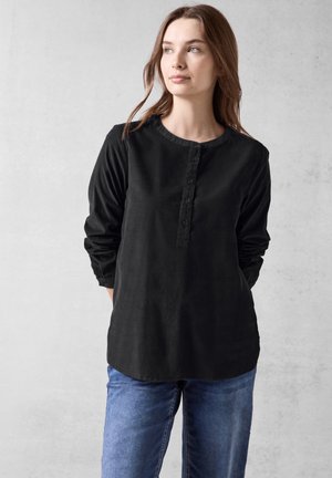 Camisa negra de manga larga con cuello redondo, botón frontal y un corte relajado, combinada con unos jeans azules.