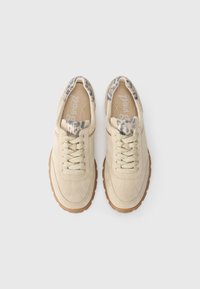 Beige semsket sko med mønstrede tekstilaksenter på tunga og kragen, beige snørebånd og gummisåler, sett ovenfra.