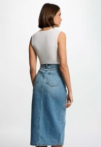 Top sin mangas de canalé gris claro combinado con una falda de mezclilla de talle alto, hasta la rodilla, en un azul claro con costuras visibles y dos bolsillos traseros.