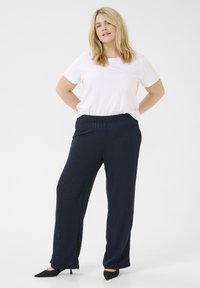 Pantalones de canalé en color azul marino con cintura elástica, combinados con una camiseta blanca sencilla. Tacones negros de punta completan el conjunto.