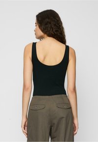 Black tank top with a scoop back; soft, stretchy material. Paired with olive-green high-waisted pants, featuring buttoned back pockets.