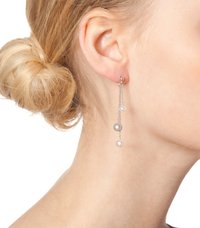 Ezüst lánc fülbevalók, melyeken három gyöngy lóg – egy szürke és két fehér –, finom textúrával és fényléssel, halvány bőrszín mellett.