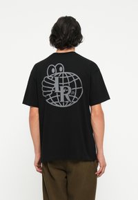 Svart bomull t-skjorte med et stort grått grafisk motiver på baksiden, som viser en globe med hender og teksten "I R ab." Korte ermer, avslappet passform.