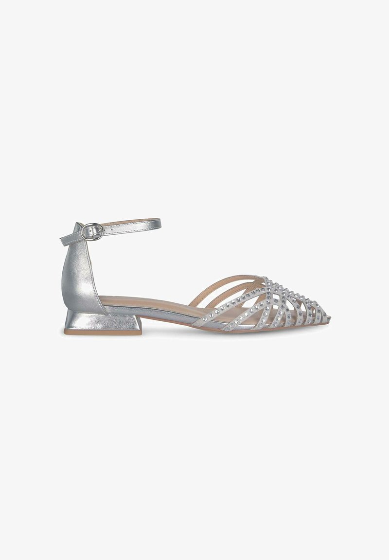 Silberne flache Schuhe mit Ankle-Strap, ausgestattet mit einem Kreuzdesign und funkelnden Edelsteinen im Zehenbereich. Strukturierte metallische Oberfläche.