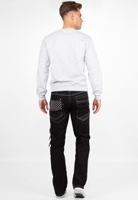 Felpa grigia con maniche lunghe, abbinata a jeans neri con cuciture decorative e design della tasca trapuntata. Sneakers bianche.