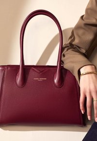 Bordeaux leren handtas met dubbele handvaten, een gladde textuur en een gouden reliëf van het logo "Isabel Bernard Paris" op de voorkant.