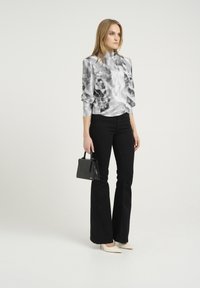 Blusa tie-dye argento e grigio con maniche lunghe e collo alto; abbinata a jeans neri a vita alta a zampa e décolleté bianchi a punta.
